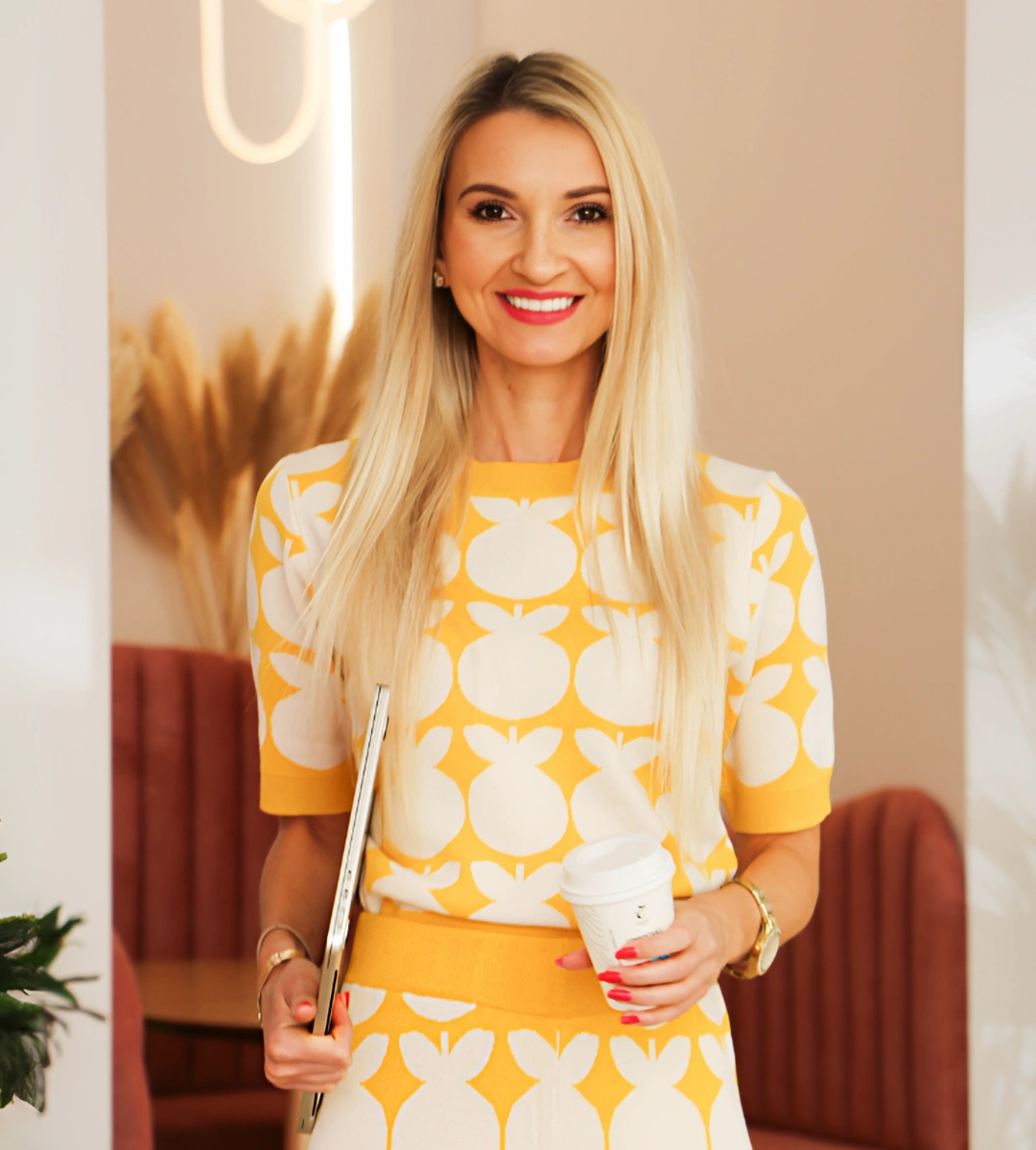 Anna at Bornfrii standing with a big smile, holding a laptop, radiating confidence and professionalism, ready to support clients in their business and leadership journey.