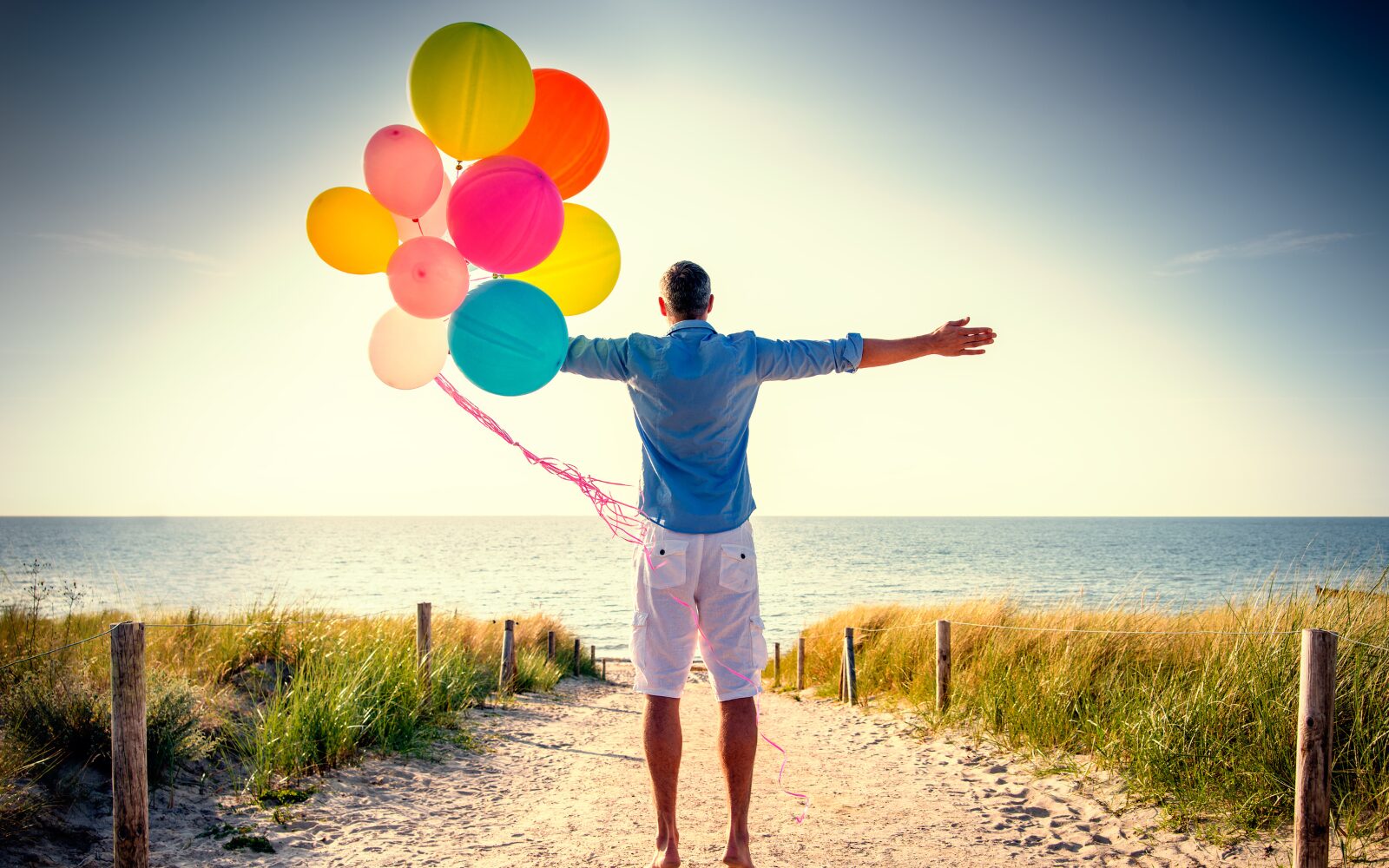 Man standing with his back to the camera, holding colorful balloons, symbolizing freedom, release, and emotional uplift.